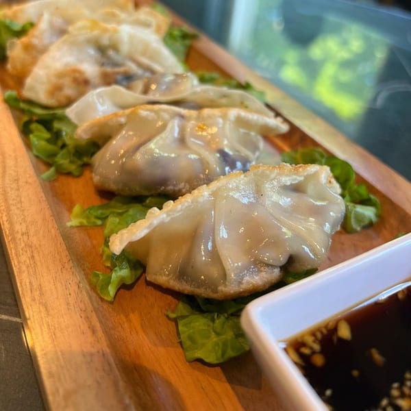 Pan-fried dumplings with crispy edges, served on lettuce with a side of soy dipping sauce.