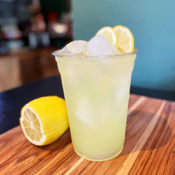 A refreshing glass of lemonade with ice and lemon slices, next to a halved lemon on a wooden board.