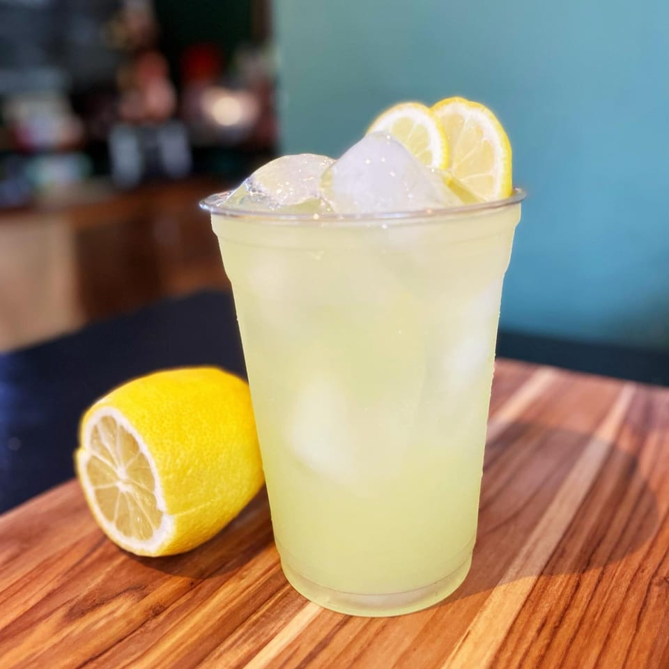 A refreshing glass of lemonade with ice and lemon slices, next to a halved lemon on a wooden board.