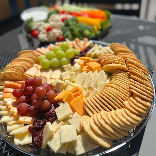 A platter of crackers, various cheeses, red and green grapes, and dried cranberries.