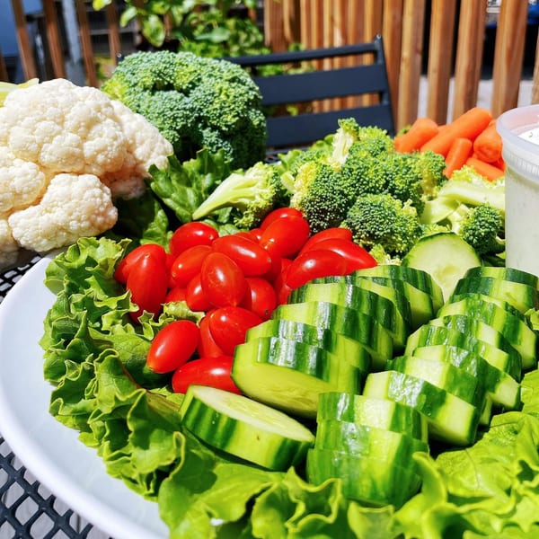 A vibrant vegetable platter with cauliflower, broccoli, carrots, cherry tomatoes, cucumbers, and lettuce.