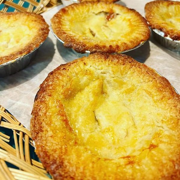 Close-up of several golden-brown, individual-sized fruit pies in foil tins on parchment paper.